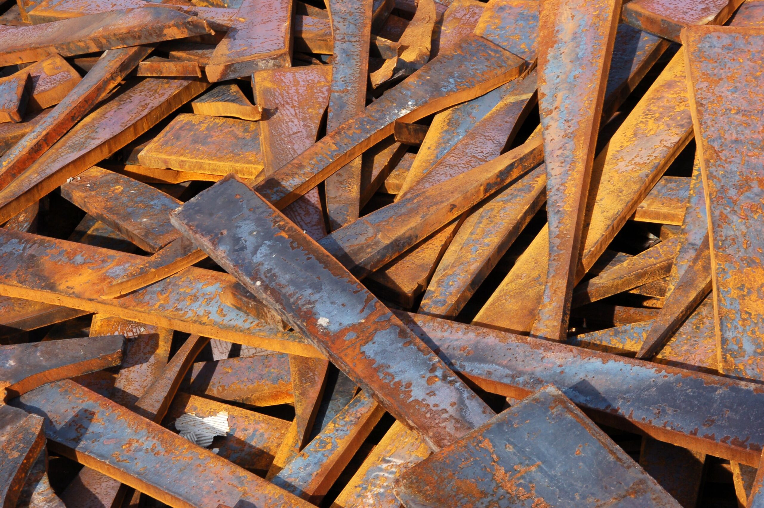 Rusty steel beams are scattered haphazardly, showcasing their weathered textures and colors, relevant for discussions on materials recycling or industrial settings.